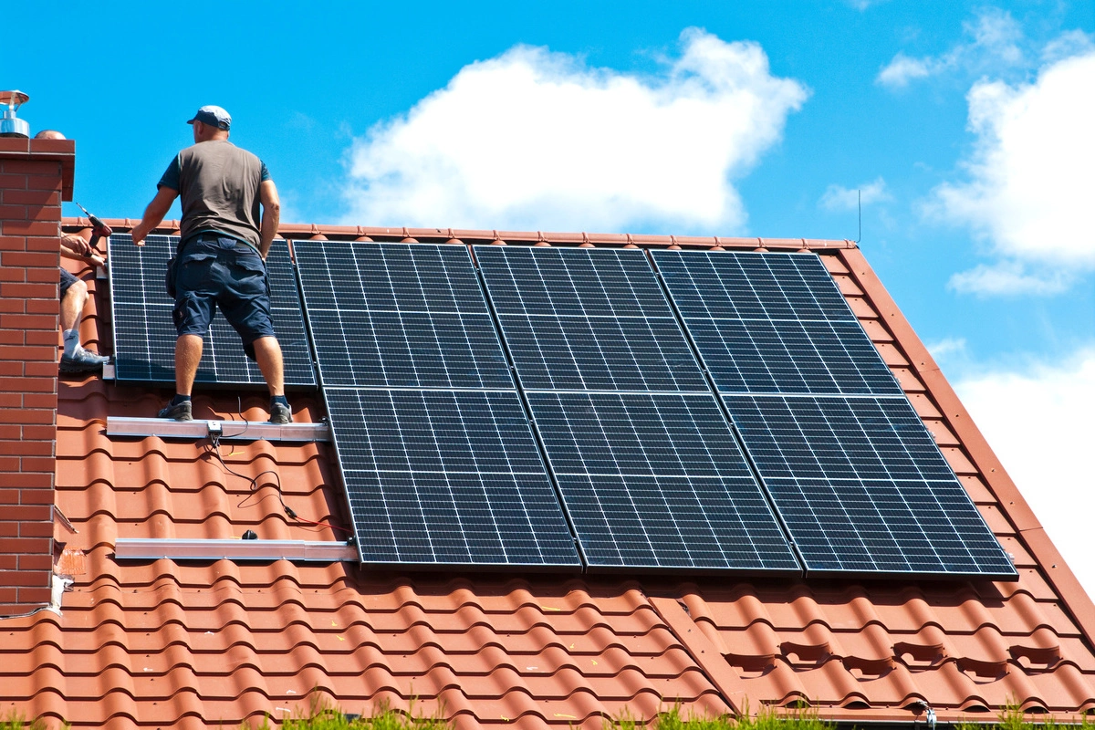 Professionnels installant des panneaux photovoltaïques sur une toiture en tuiles rouges